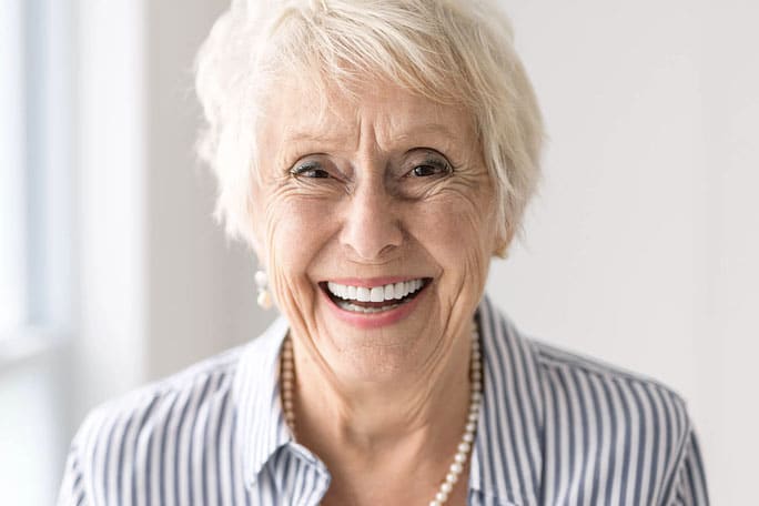 Older woman smiling confidently, representing patients choosing ceramic dental implants