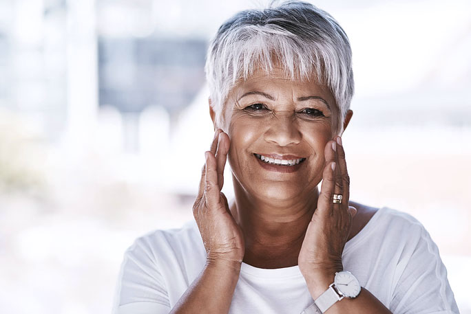 Older woman smiling with hands on her cheeks, representing metal-free implant options
