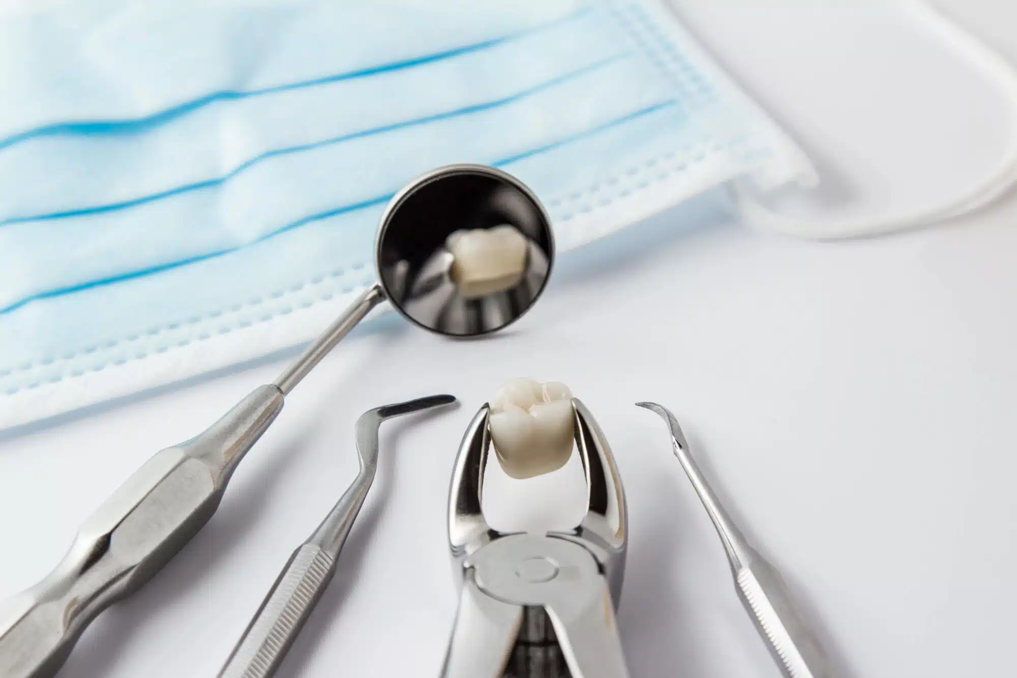 Dental extraction forceps holding a tooth beside dental instruments and a mask